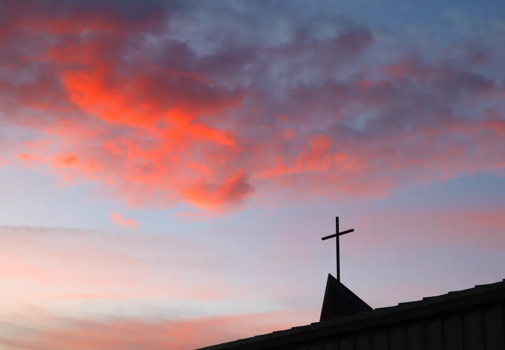 Sunrise clouds over the cross of a church.